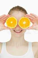 Close up of a woman placing oranges on her eyes