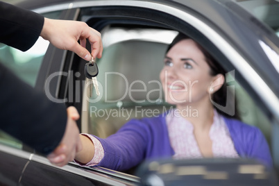 Woman in a car while shaking a hand and receiving car keys