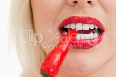 Blonde woman biting a red chili pepper