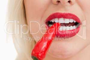 Blonde woman biting a red chili pepper