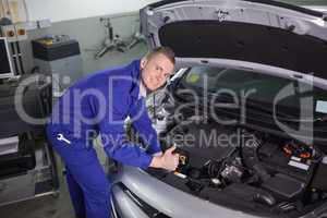 Smiling mechanic leaning on a car with his thumb up