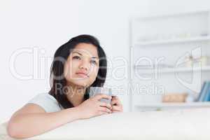 Woman holding a mug as she rests one arm on a sofa