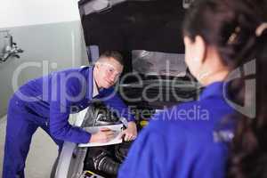 Mechanic leaning on a car looking at a colleague