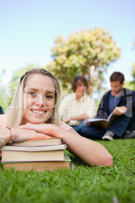 Close-up of a girl lying head on her books in a park