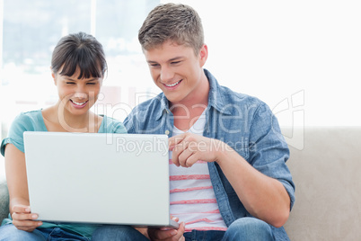 A pretty couple sitting while using a laptop together
