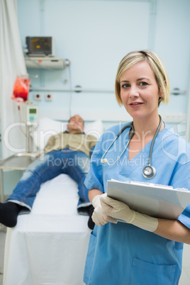 Nurse next to a male patient while holding a clipboard