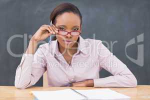 Serious teacher sitting at desk while touching her glasses