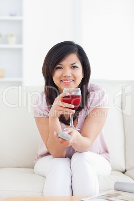 Woman holding a television remote while holding a glass of red w
