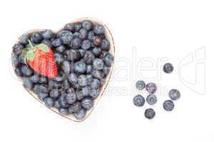 One strawberry and bluberries in  a heart shaped bowl