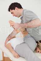 Serious osteopath stretching the leg of his patient