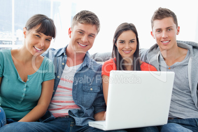 A smiling group of friends sitting together with a laptop as the