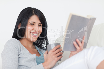 Woman smiling while holding a grey mug and a book
