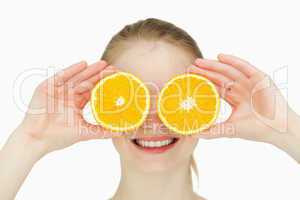 Close up of a smiling woman placing oranges on her eyes
