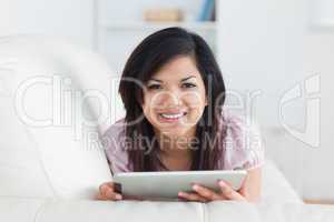 Woman smiling while resting on a couch and playing with a tablet