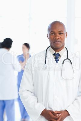 Doctor standing upright with his hands crossed and his team in t