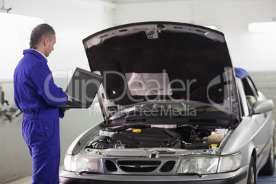 Mechanic typing on a computer next to a car