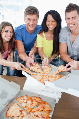 Smiling friends taking some pizza as they look at the camera