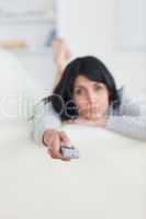 Woman laying on a sofa while pressing on a remote