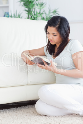 Woman sitting on the floor in front of a couch while reading a b