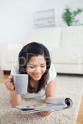 Woman lays on the floor as she holds a mug and a magazine