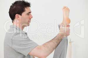 Brown-haired chiropractor stretching the leg of his patient