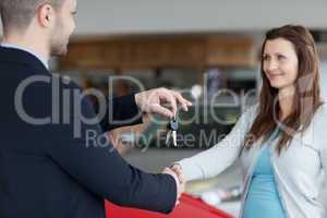 Salesman giving car keys while shaking hand of a woman