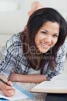 Woman smiling as she lays on the floor and writes on a notebook