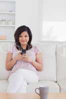 Woman sitting on a sofa while she is holding a phone