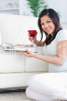 Smiling woman holding a glass of red wine and a magazine