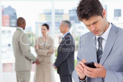 Young serious manager using his cell phone to send a text