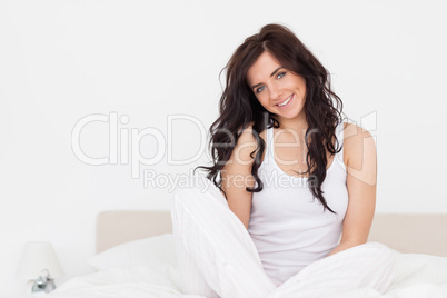 Cheerful brunette woman sitting on her bed