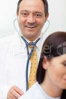 Smiling doctor auscultating a patient