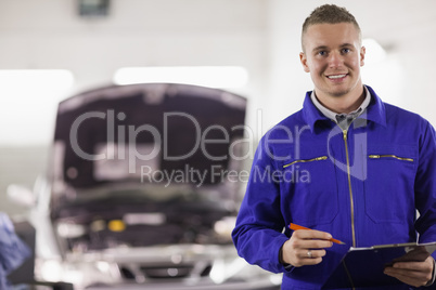 Mechanic holding a clipboard and a pen next to a car