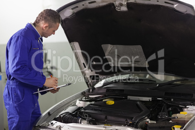 Mechanic holding a clipboard while looking at a car engine