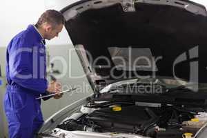Mechanic holding a clipboard while looking at a car engine