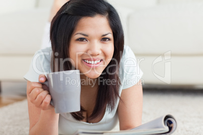 Smiling woman on the floor holding a mug and a magazine
