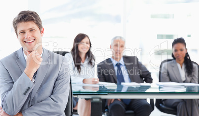 Smiling young executive sitting in front of his team with his ha