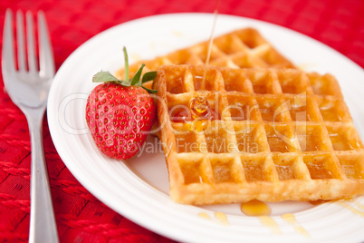 Waffles and syrup and strawberry together in a white plate