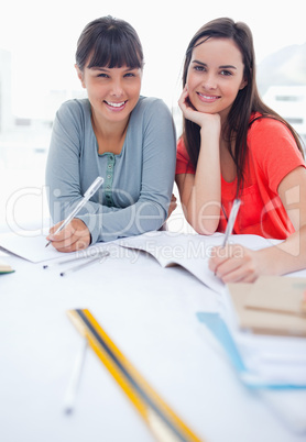 A pair of smiling girls looking at the camera as they work on sc