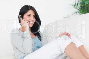 Woman smiling and phoning while sitting on a sofa
