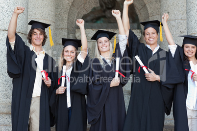 Smiling graduates posing while raising arms