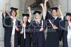 Smiling graduates posing while raising arms