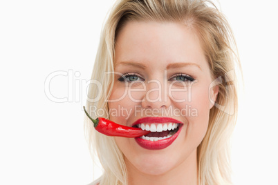 Happy woman biting a red chili while standing