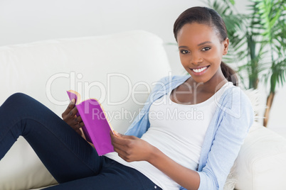 Black woman sitting on a sofa while holding a book