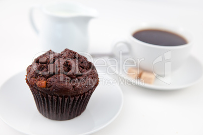 Chocolate muffin and a cup of coffee on white plates with sugar