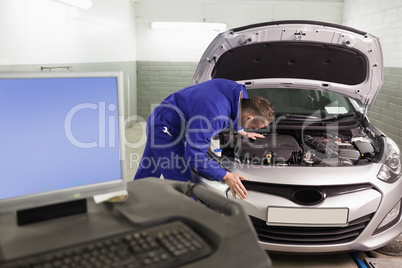 Mechanic repairing a car next to a computer