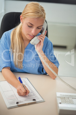 Nurse calling while writing on a clipboard