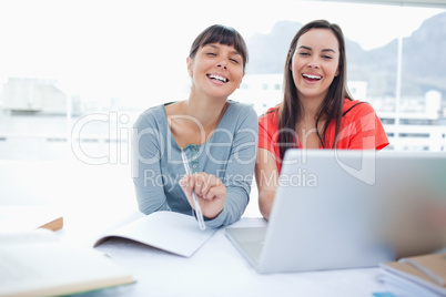 Two laughing girls sitting in front of a laptop together as they