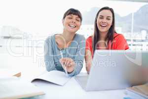 Two laughing girls sitting in front of a laptop together as they