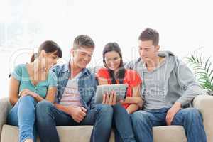 A group of friends sit on the couch while watching a tablet pc